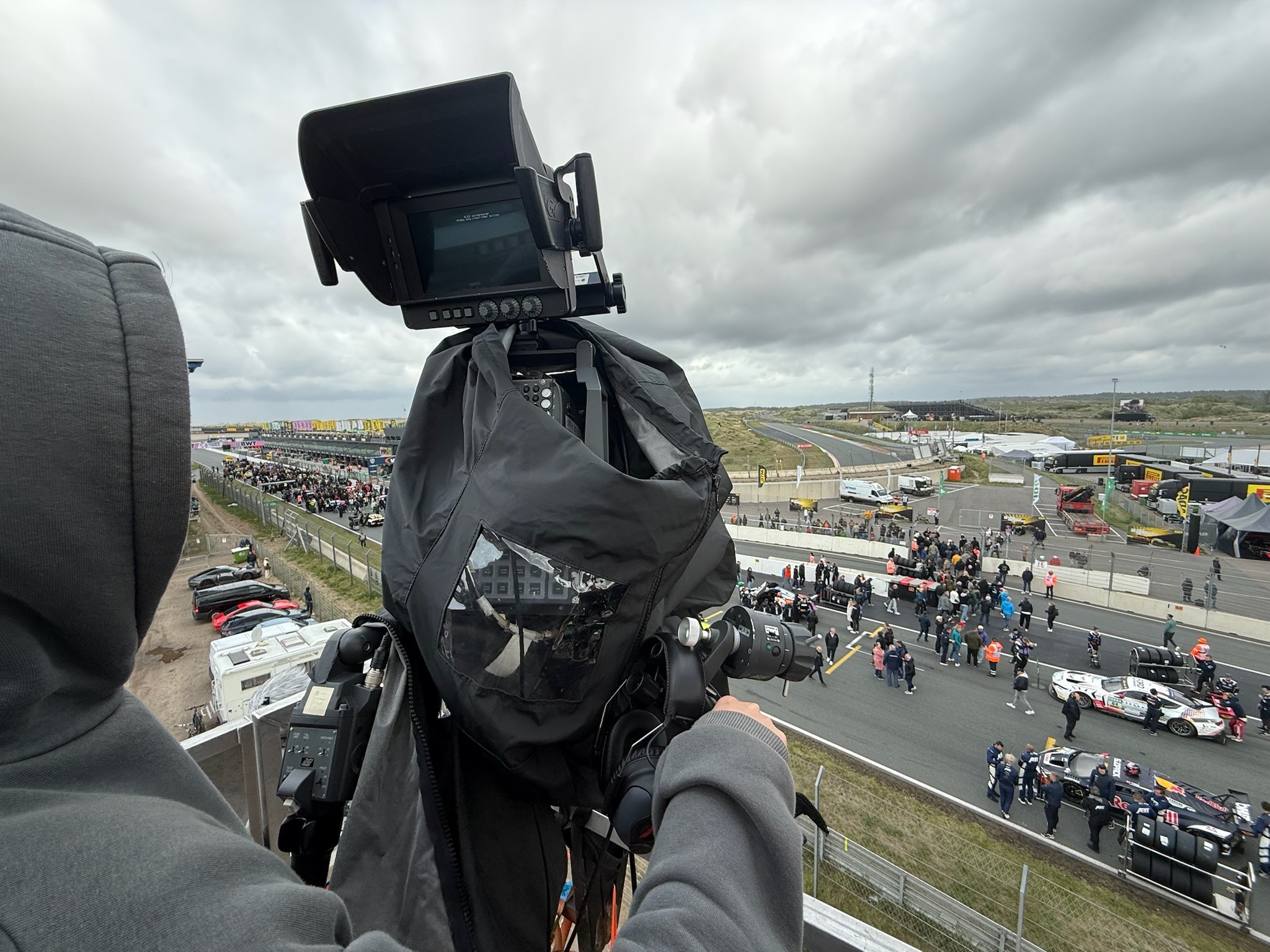 TV-Kameramann filmt das Fahrerlager einer Rennstrecke von einem erhoehten Standpunkt - Live-Media-Produktion von Nik Pottbecker